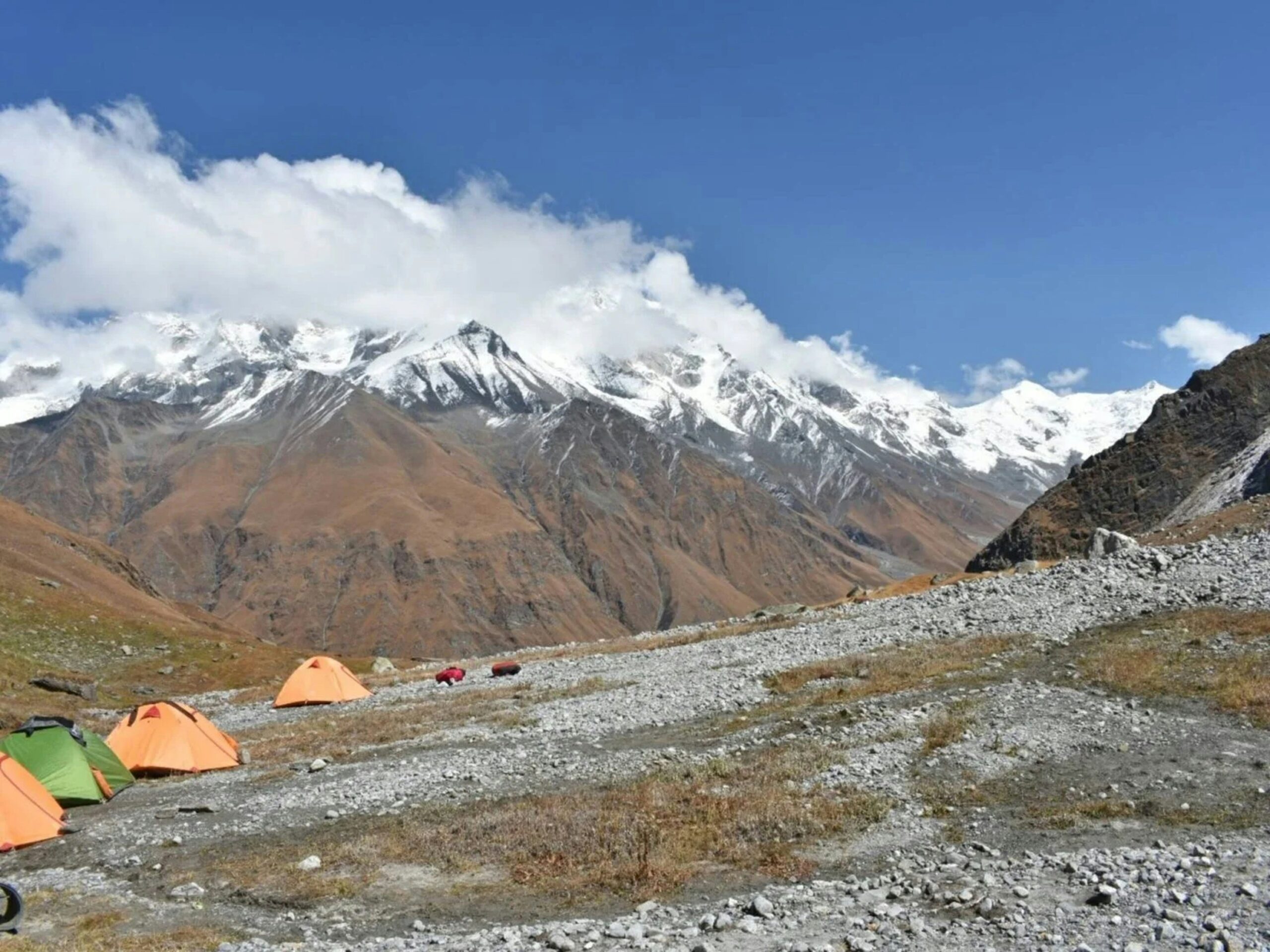 Tents pitched at a rocky high altitude campsite with snow covered Himalayan mountains during Bali Pass Trek